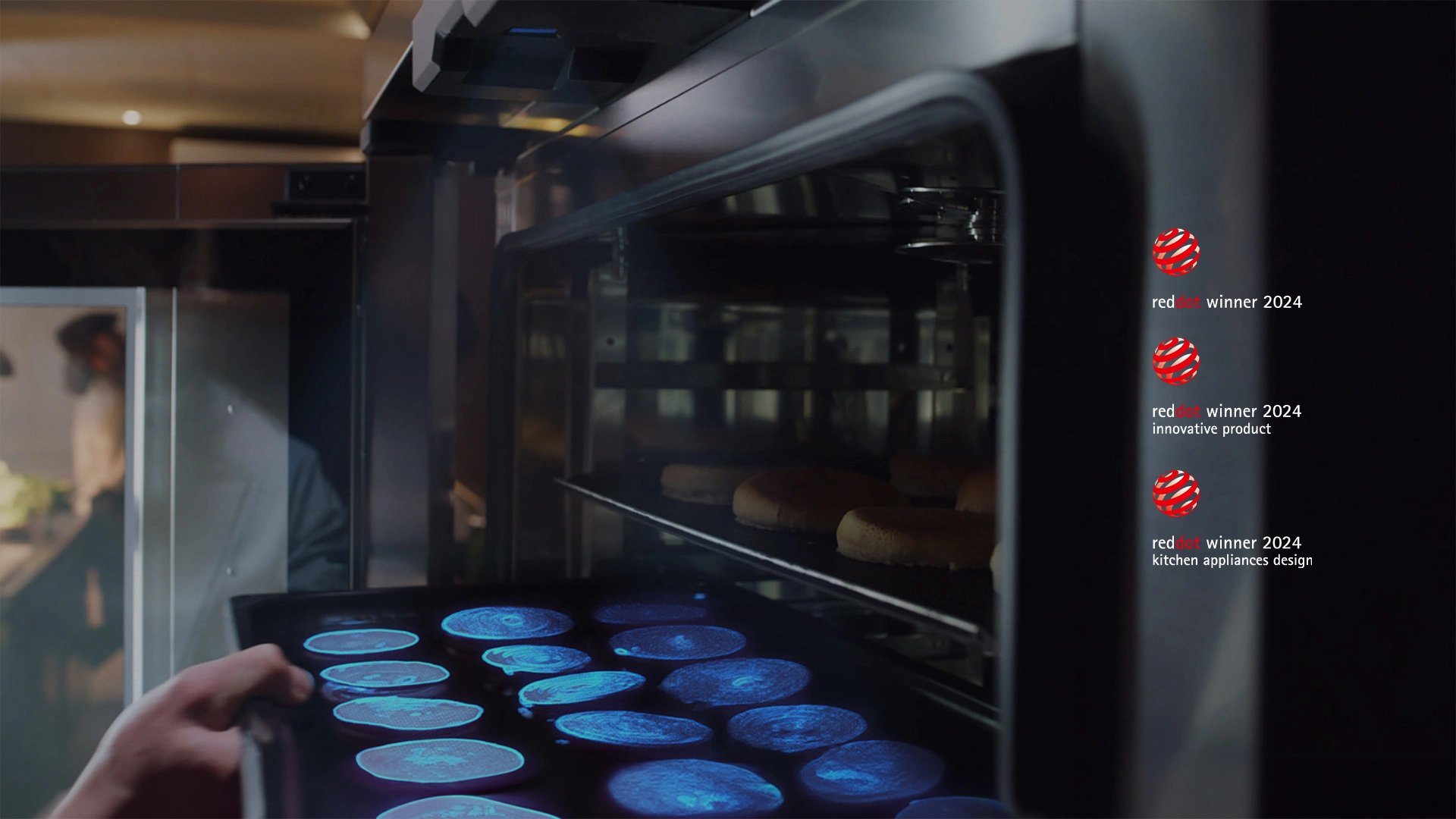 Uma mão colocando uma bandeja de alimentos dentro do forno. Um sensor no topo emite uma luz azul para escanear e identificar o alimento.