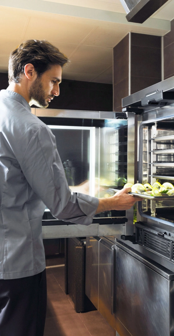 Um chef na cozinha abre a porta do forno combinado e coloca uma bandeja com peixe e limão no forno.